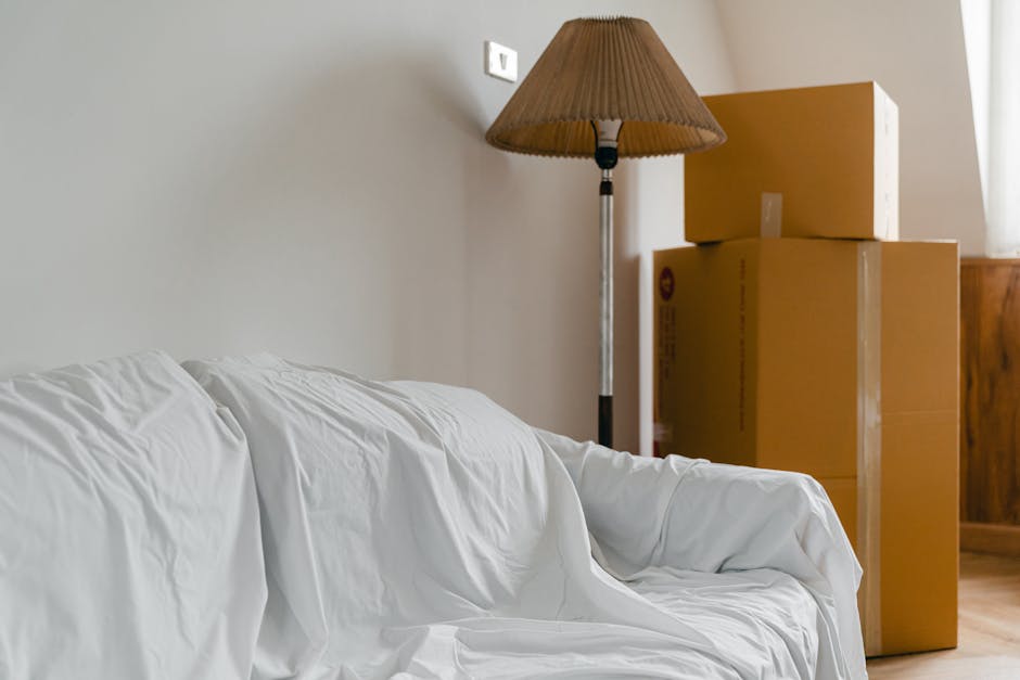 A cardboard moving box with bold black text reading 'FRAGILE MIRROR OR GLASS' and 'DO NOT SLAY FLAT' is placed on a wooden floor with visible wood grain, knots, and typing marks. The box appears to be