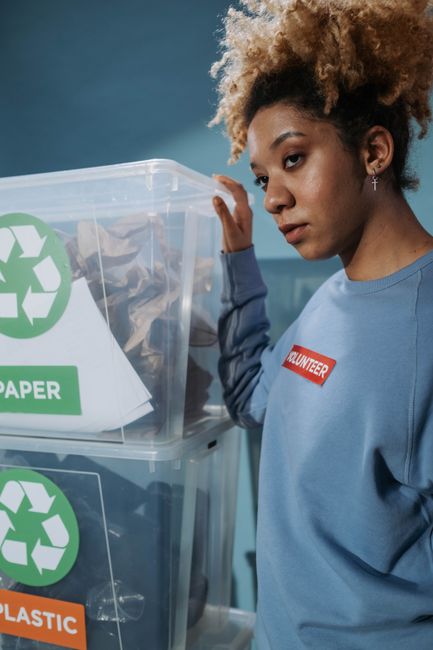 A clear plastic container placed on a table during a home relocation briefing, prominently displaying recycling symbols for paper and plastic. The container is partially filled with used plastic packa